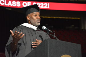 Keith Dawkins '94 in a cap and gown at the podium addressing the Class of 2022 at the СƵ Commencement
